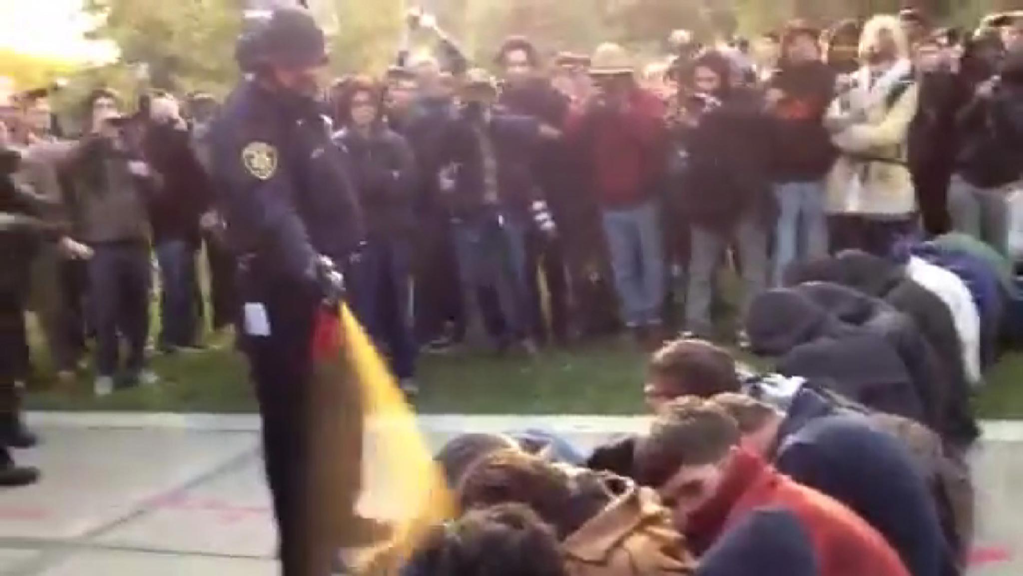 In this image made from the video, a police officer uses pepper spray as he walks down a line of Occupy demonstrators sitting on the ground at the University of California, Davis