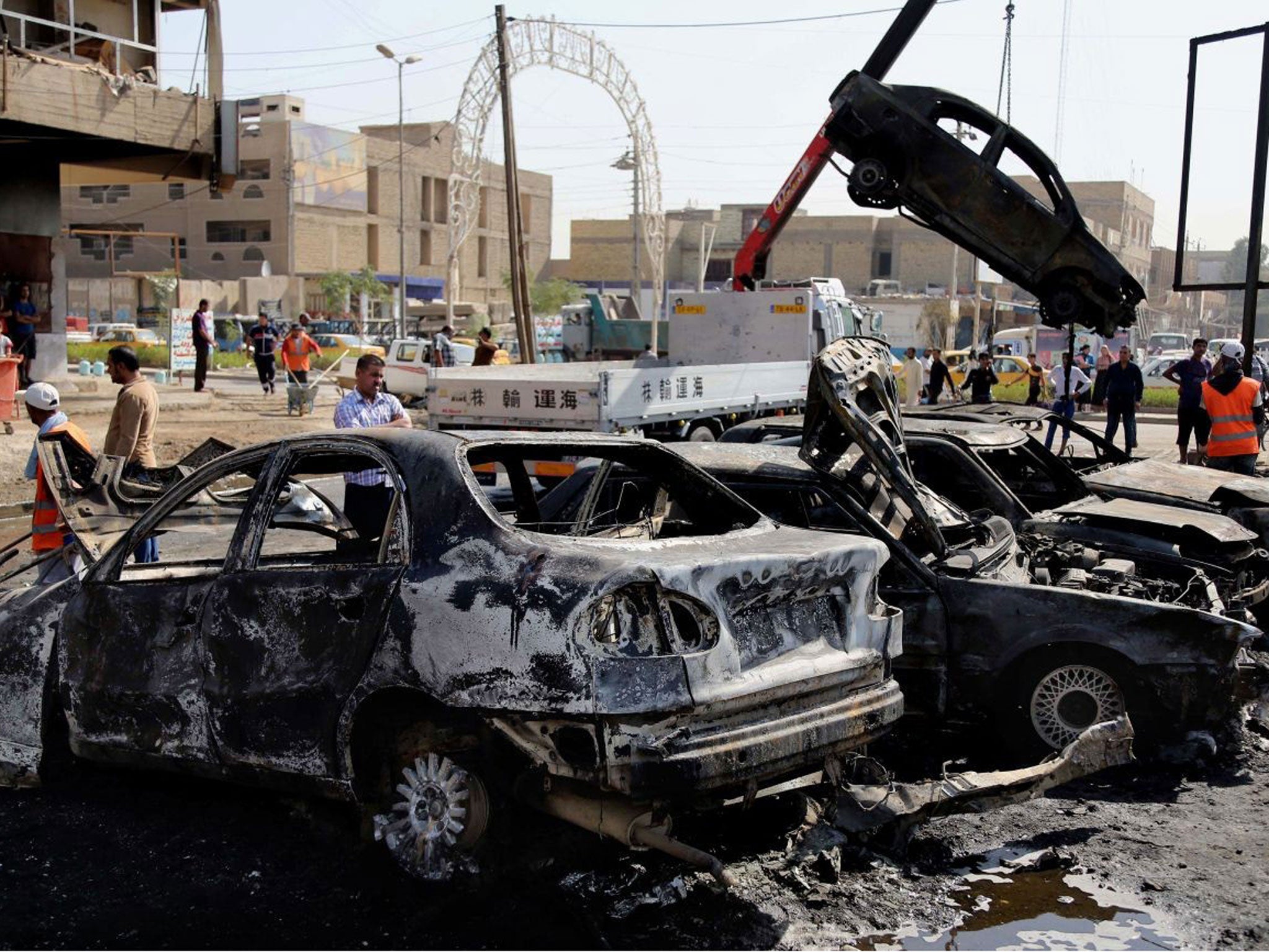 A crane lifts away a burned car at the site of a car bombing in the Sha'ab neighborhood of Baghdad on Sunday 27 October, 2013