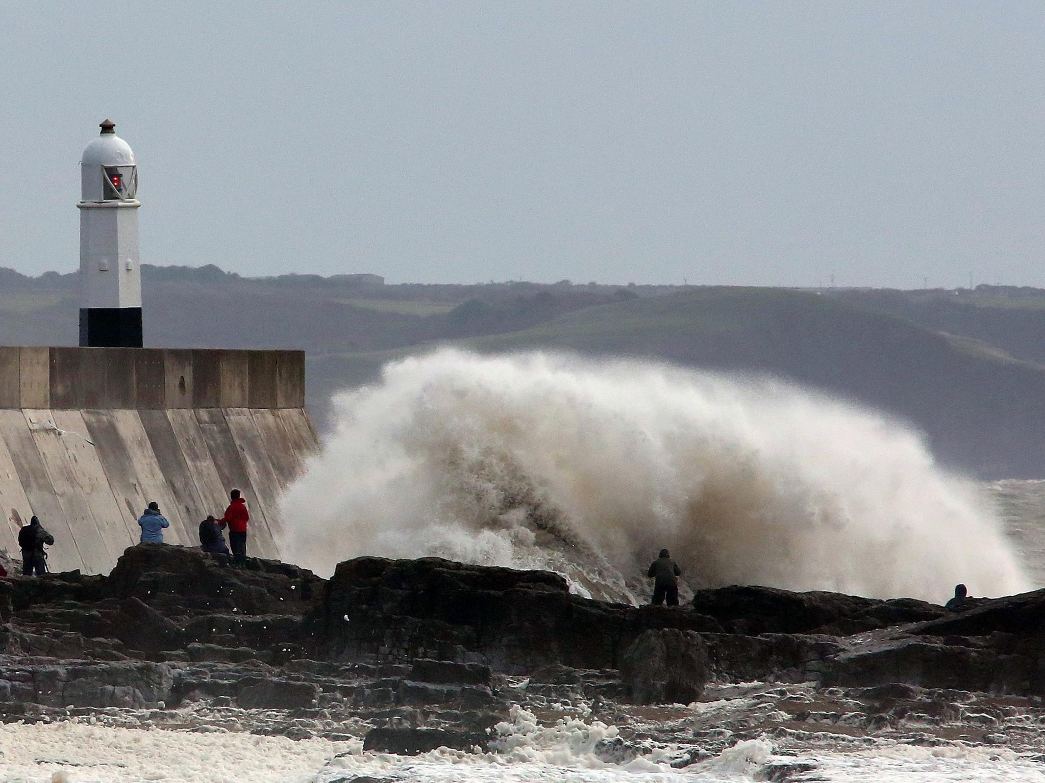 People stand on the sea wall at Porthcawl, south Wales, as heavy seas pound the harbour