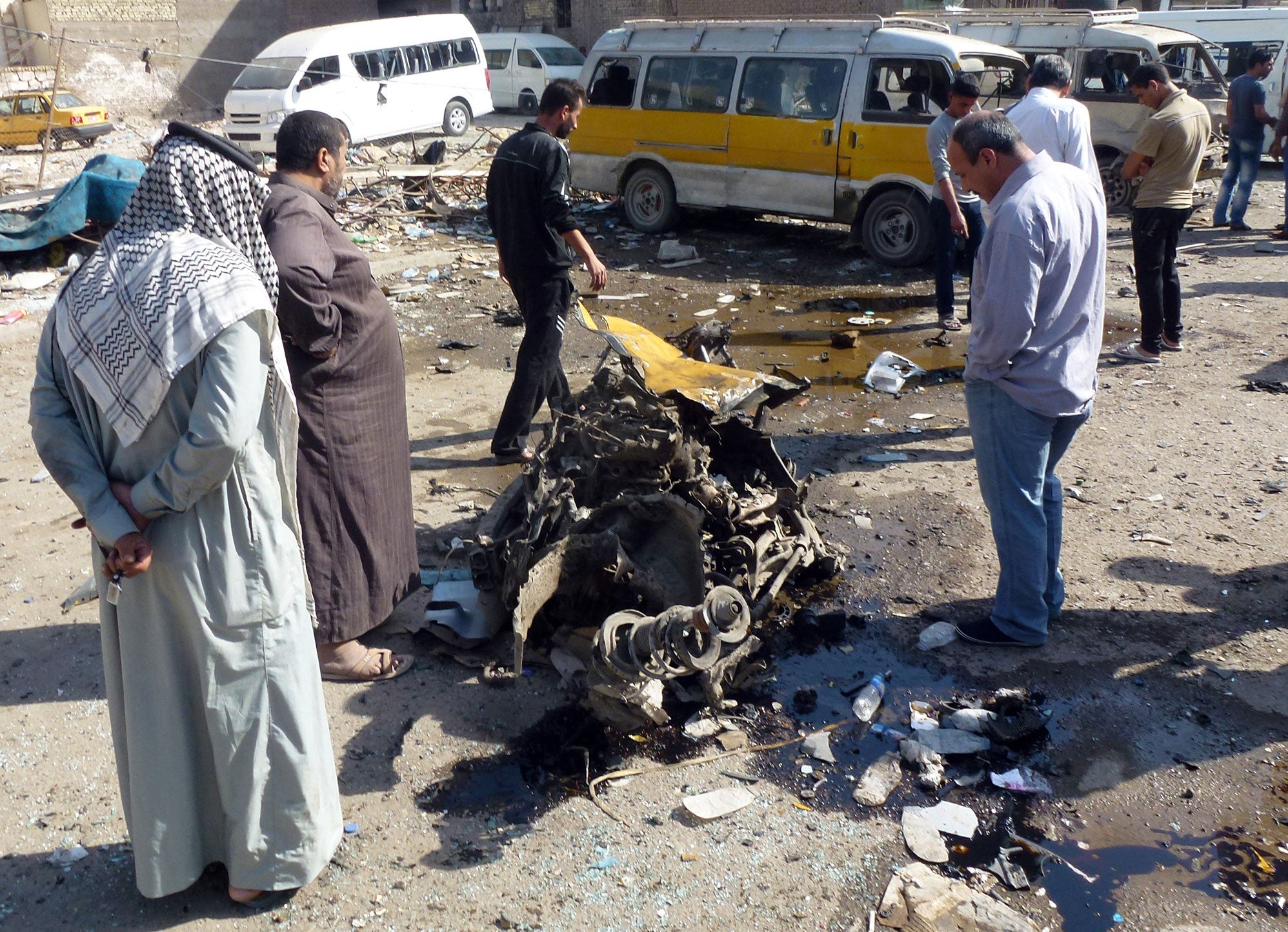 Iraqis look at the remains of a vehicle following an explosion at a small bus station on October 27, 2013, in the the Mashtal district of the capital Baghdad