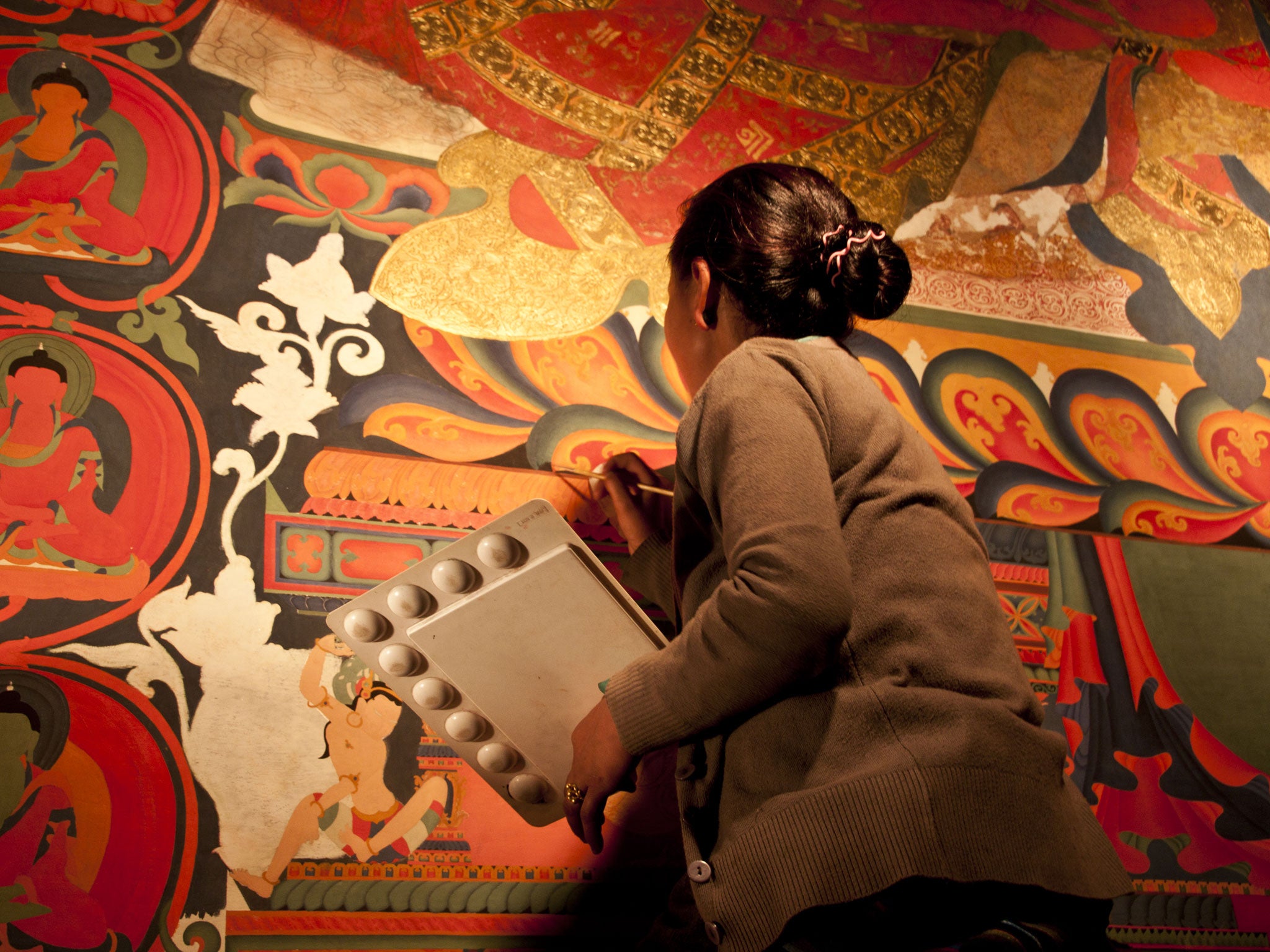 A local woman retouches a Buddhist mural
