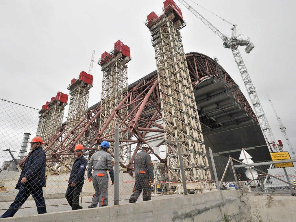 Workers walk by a shelter and containment area built over the destroyed 4th block (Getty)