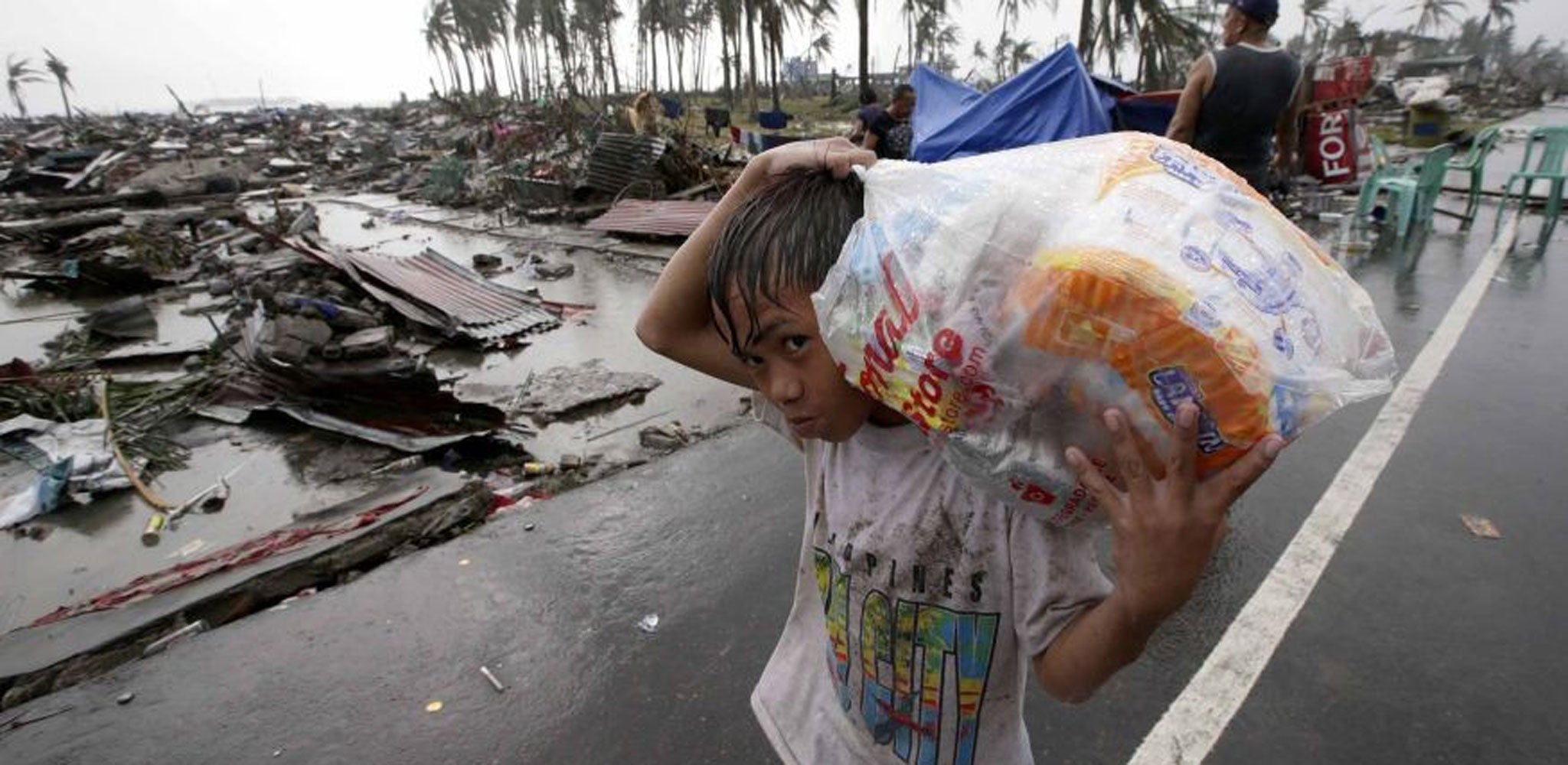 A boy carries relief goods, walking past the devastation caused by Typhoon Haiyan, in Tacloban city, Leyte province, central Philippines