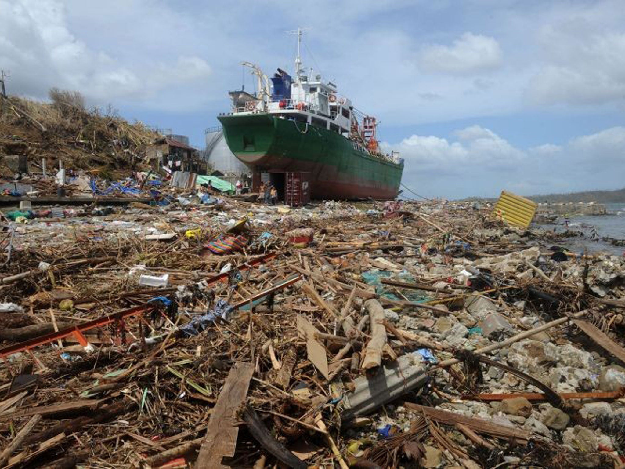 People walk amongst debris next to a ship washed ashore in the aftermath of Super Typhoon Haiyan at Anibong in Tacloban