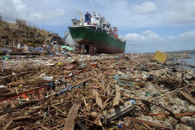 People walk amongst debris next to a ship washed ashore in the aftermath of Super Typhoon Haiyan at Anibong in Tacloban