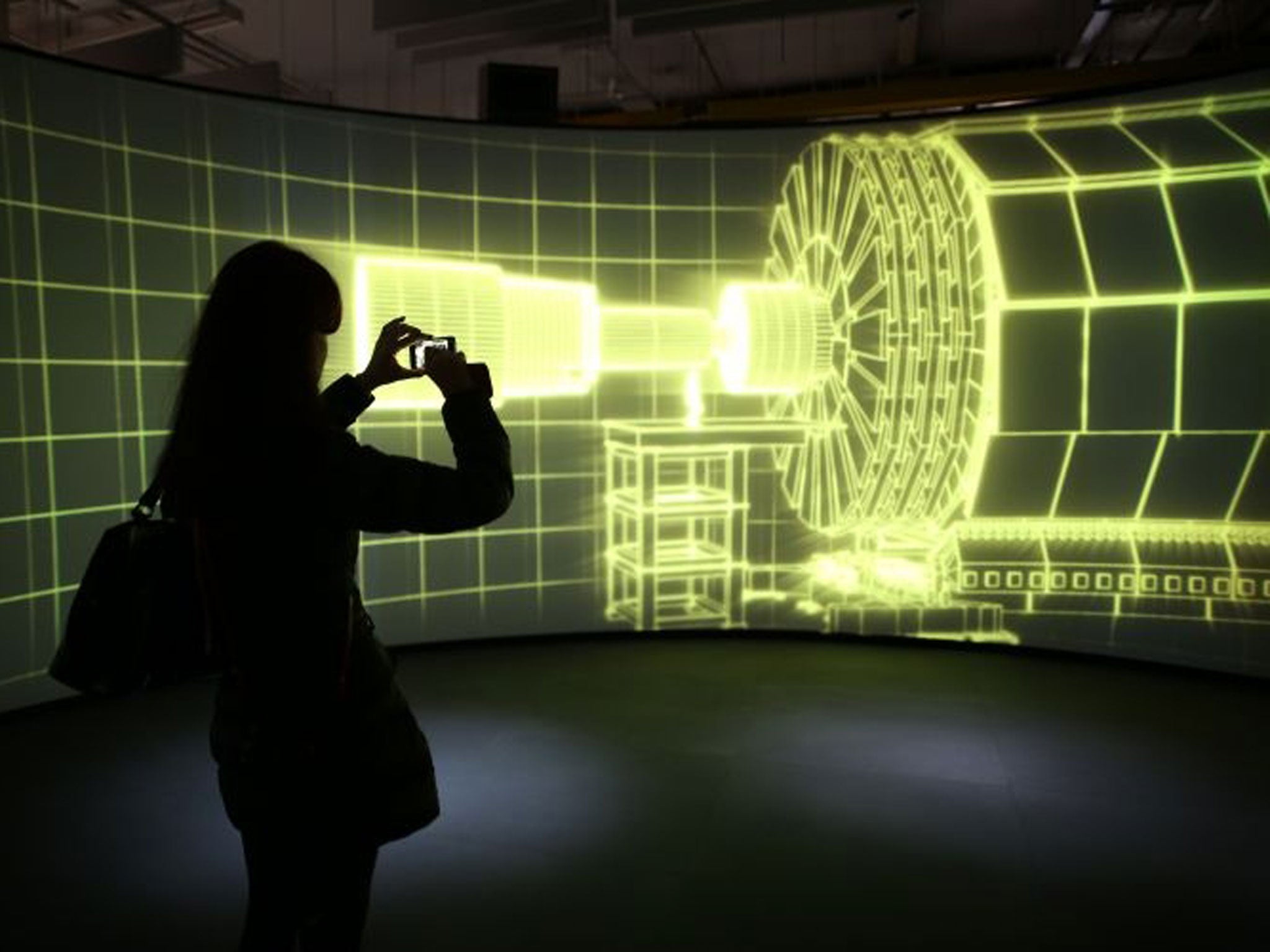 A visitor to the Science Museum takes a phone photograph of a video projection showing the workings of the Large Hadron Collider at the 'Collider' exhibition