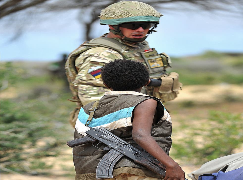 A young Somali boy with an AK-47 rifle talks to a British soldier in July 2012