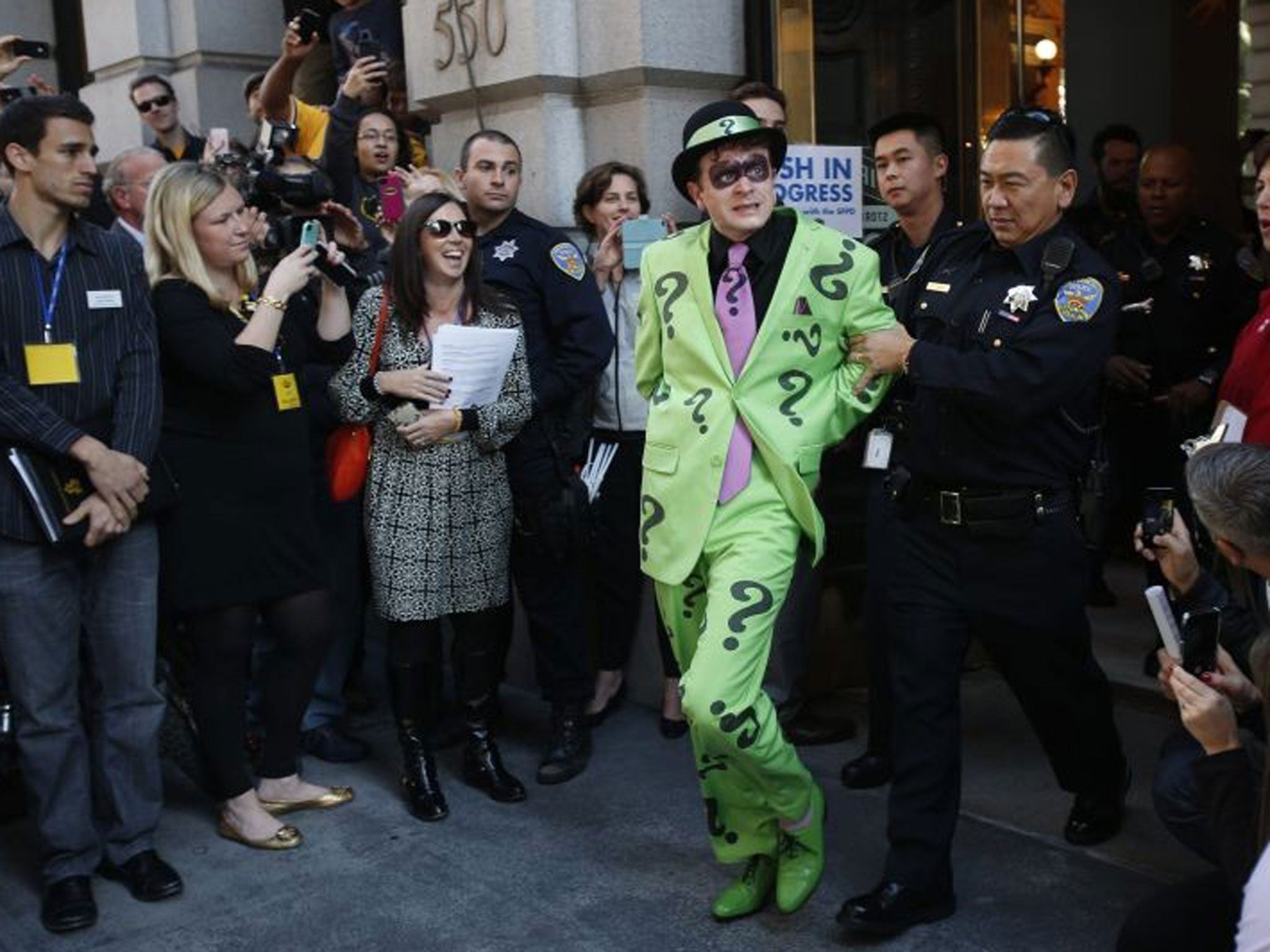 The Riddler is taken away by a San Francisco police officer after being apprehended by