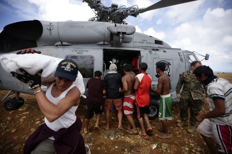Typhoon victims queue to get  relief aid from a US Navy Sea Hawk helicopter in the typhoon-devastated remote  island of Manicani, Guiuan Eastern Samar island province