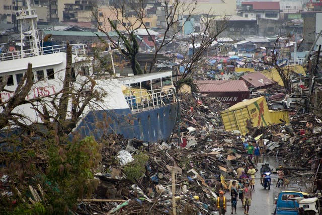Displaced residents walk alongside a ship that was washed ashore by Super Typhoon Haiyan and is now lodged among the rubble of destroyed homes in Tacloban