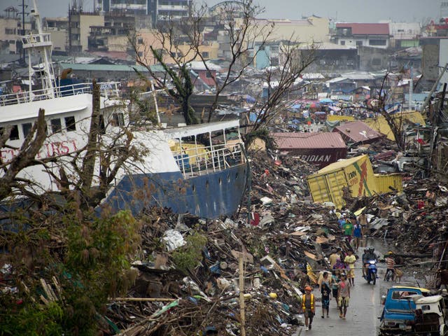 Displaced residents walk alongside a ship that was washed ashore by Super Typhoon Haiyan and is now lodged among the rubble of destroyed homes in Tacloban