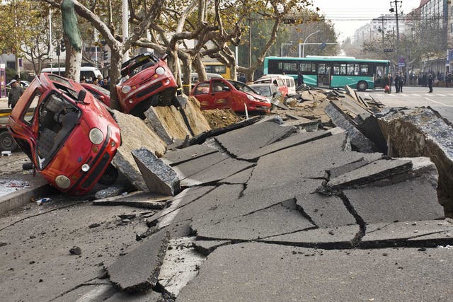Damaged vehicles lie by a street after an oil pipeline exploded, ripping roads apart, turning cars over and sending thick black smoke billowing over the city of Qingdao