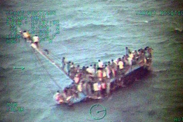 A handout picture made available by the US Coast Guard and taken from a Coast Guard helicopter shows some 100 Haitians sitting on the hull and mast of a sail freighter after it grounded and capsized off the coast of the Bahamas