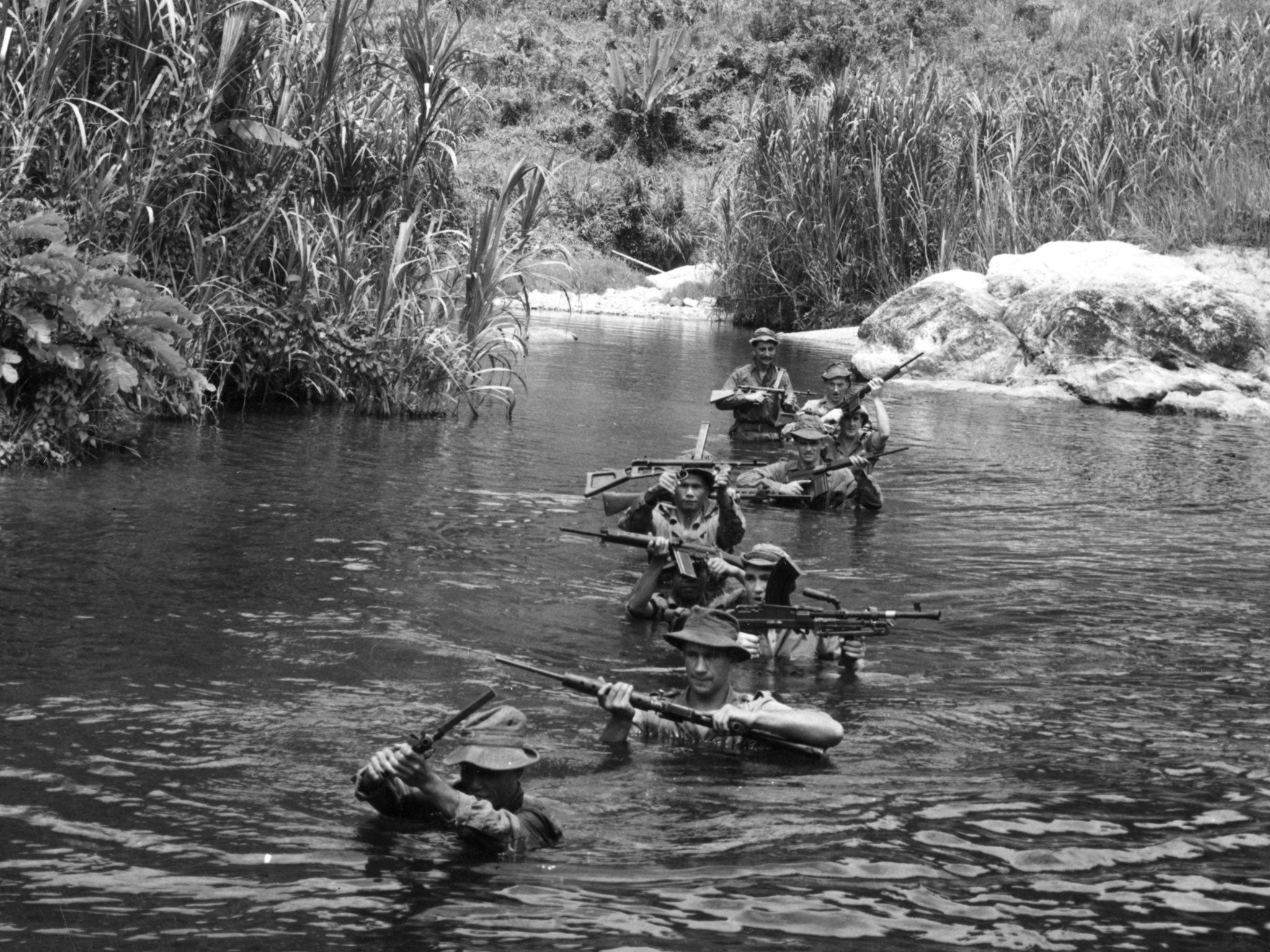 1957: Soldiers on patrol holding their guns above their heads as they wade up a river in the jungle during the Malayan Emergency