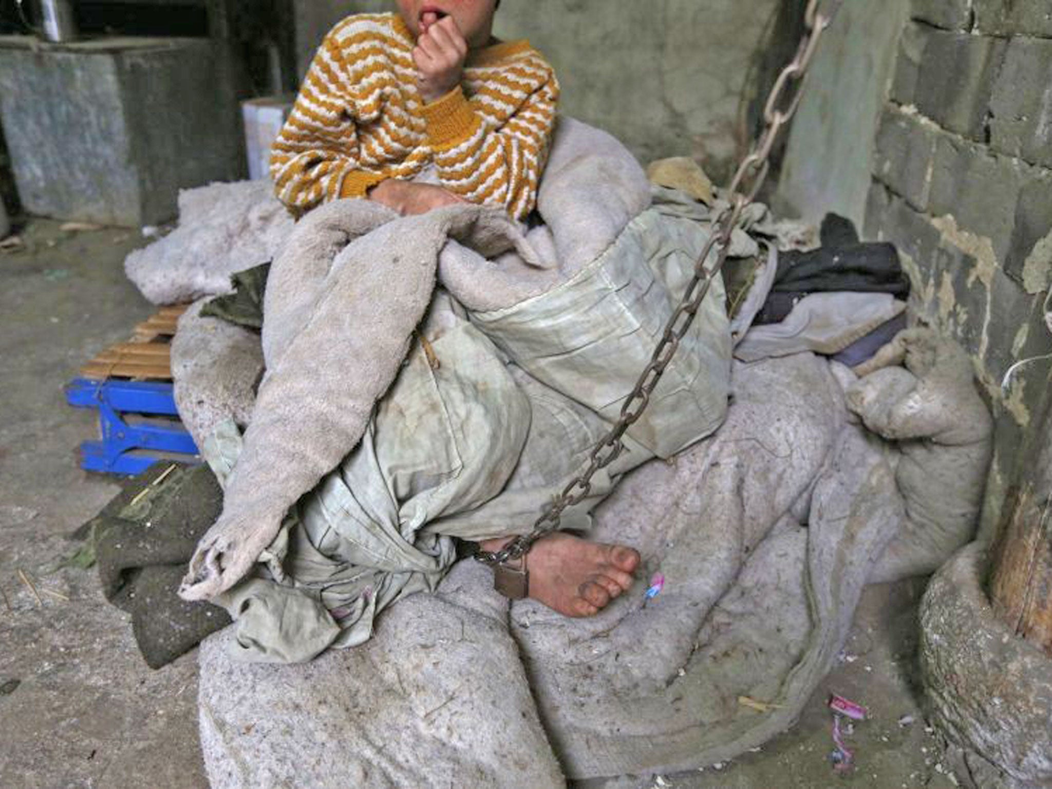 Eleven-year-old He Zili sits as he is chained to a pillar at his home in Zhejiang province