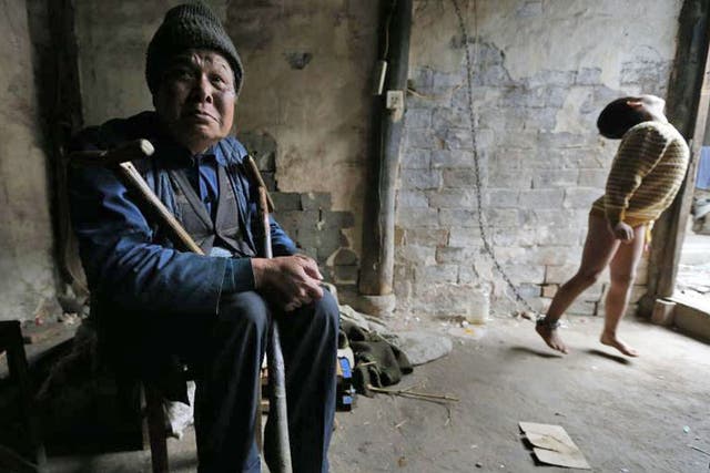 He Zili, 11, is seen chained to a wall as his grandfather sits next to him at their home in Zhejiang province