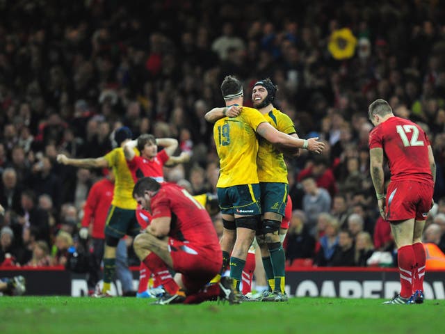 A disconsolate Wales team can't bare to look as Australia celebrate their win at the Millennium Stadium