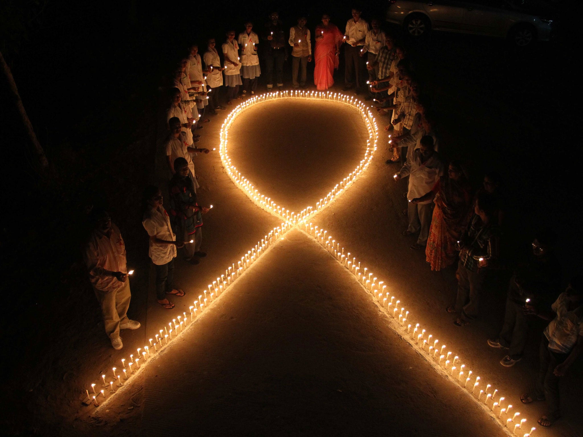 Nursing students and medical staff hold candles and stand by a formation in the shape of a red ribbon, the universal symbol of awareness and support for those living with HIV, made with candles