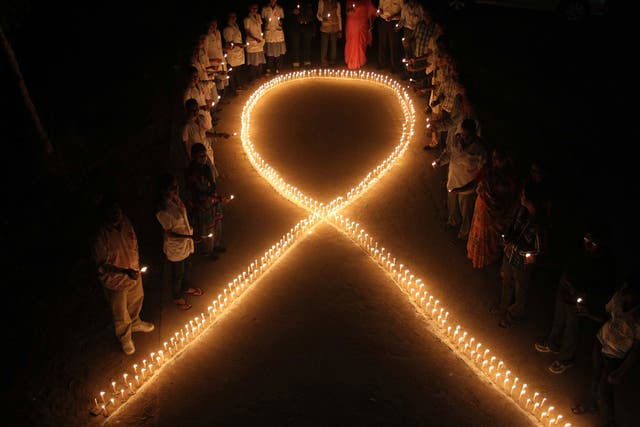 Nursing students and medical staff hold candles and stand by a formation in the shape of a red ribbon, the universal symbol of awareness and support for those living with HIV, made with candles