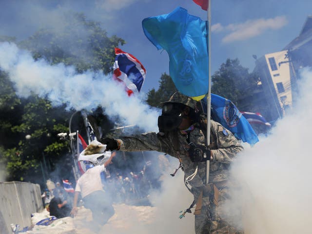 A protester throws back a tear-gas canister during clashes with police near Government House in Bangkok