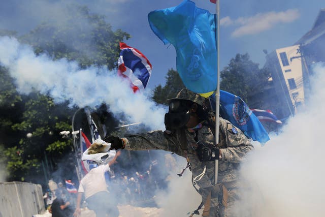 A protester throws back a tear-gas canister during clashes with police near Government House in Bangkok