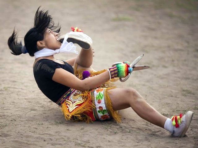 A 'scissors' dancer grabs her shoe with her mouth while performing in a national scissors dance competition in the outskirts of Lima, Peru