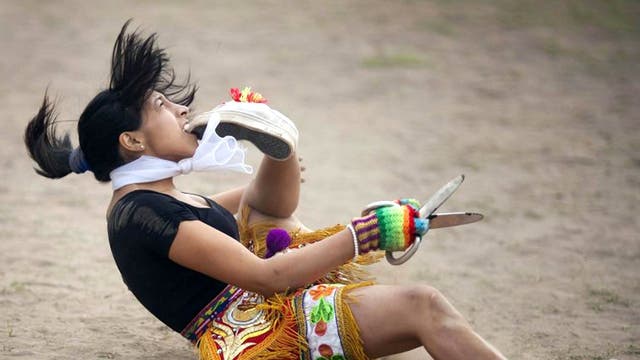 A 'scissors' dancer grabs her shoe with her mouth while performing in a national scissors dance competition in the outskirts of Lima, Peru