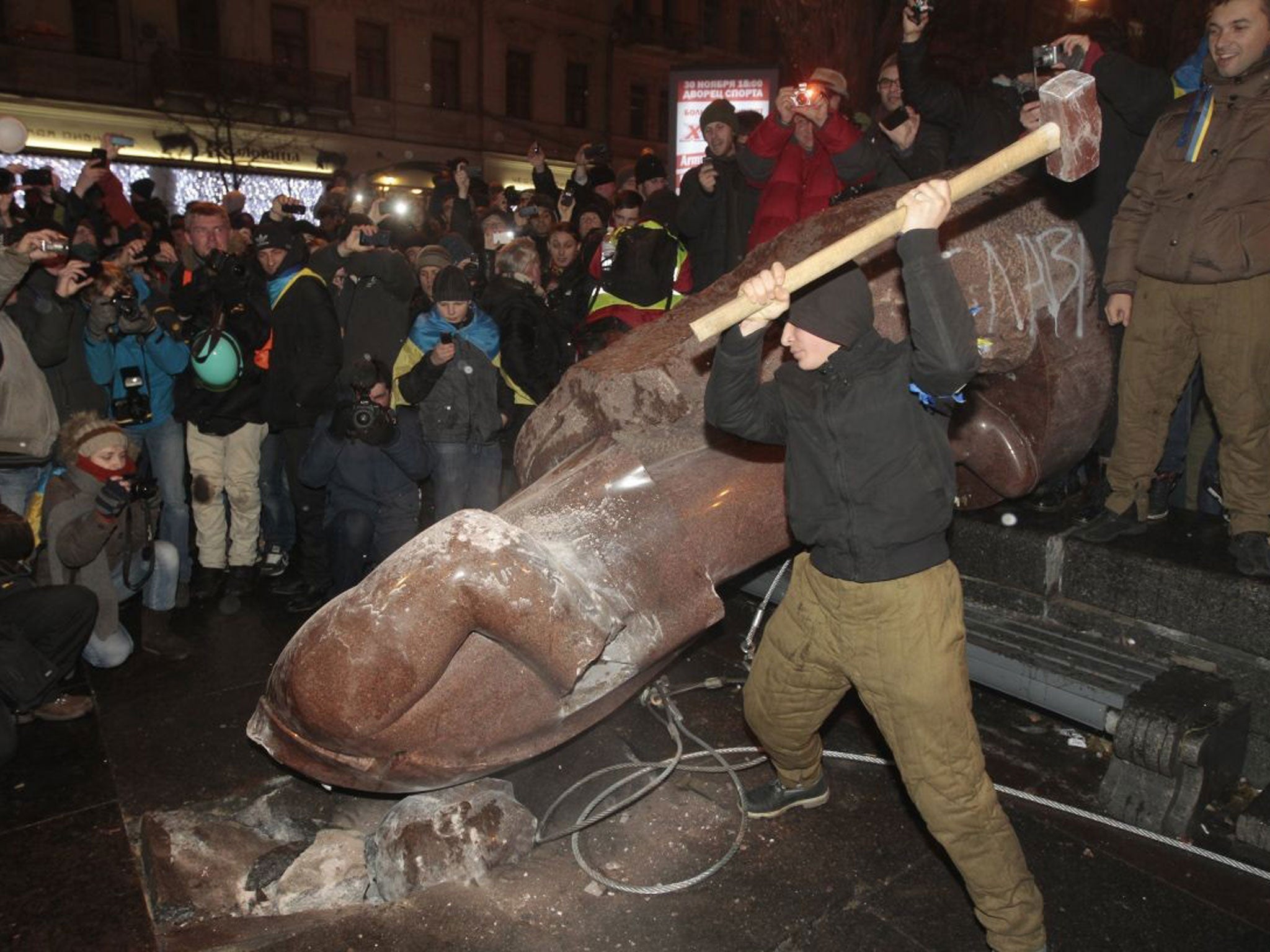 An anti-government protester beats the statue of Vladimir Lenin with a sledgehammer during a rally in Kiev