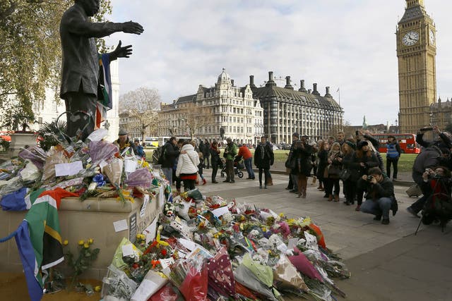 People gather to look at flowers and tributes left at the statue of Nelson Mandela in Parliament Square, London