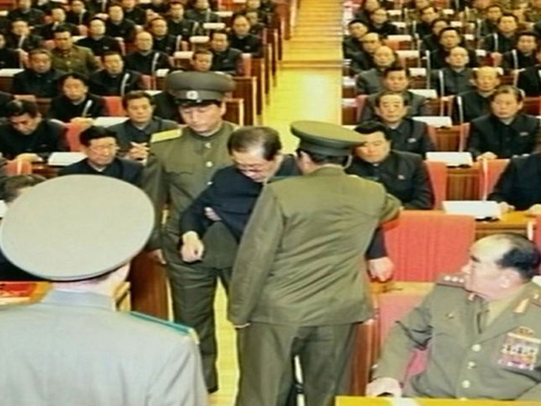Jang Song-Thaek being dragged out from his chair by two police officials during a meeting in Pyongyang
