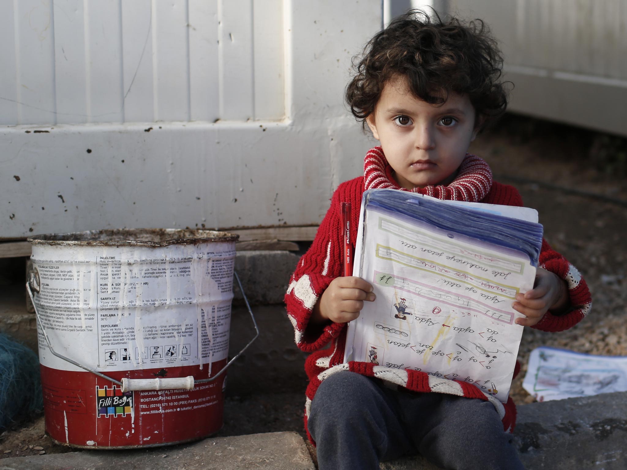 Three-year-old Aisha Nour from Azaz, Syria, reads outside the container in which she lives