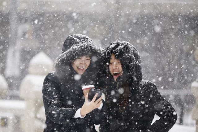 Women smile as they look at a picture on a mobile phone during snowfall in winter in central Seoul