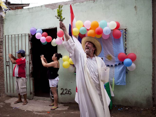Padre Toto de Vedia blesses residents with holy water using an olive branch during a procession celebrating Paraguay's patroness, 'Our Lady of Caacupe', commonly called the 'Blue Virgin' in a slum of Buenos Aires, Argentina.  Padre Toto is one of many slum priests who Pope Francis has long supported. He led thousands in this year's procession that winds through every corner of their slum