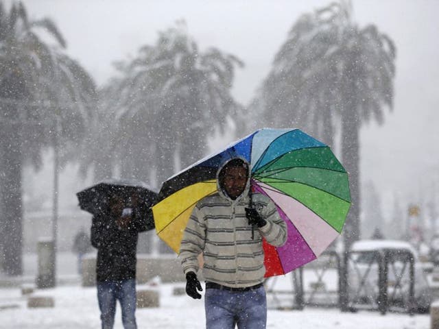 Men holding umbrellas walk outside Jerusalem's Old City during snowfall. Snow fell in Jerusalem and parts of the occupied West Bank where schools and offices were widely closed and public transport was paused