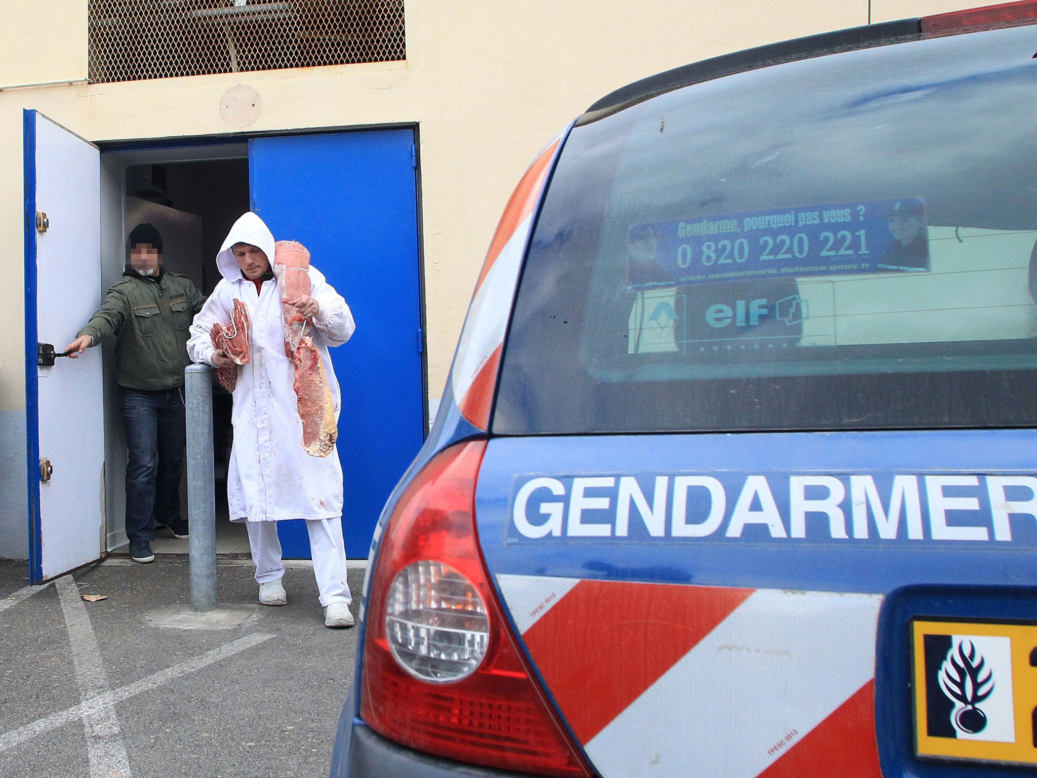 A requisitioned employee carries pieces of meat under the surveillance of a policeman at a butchery's depot in Narbonne, southern France