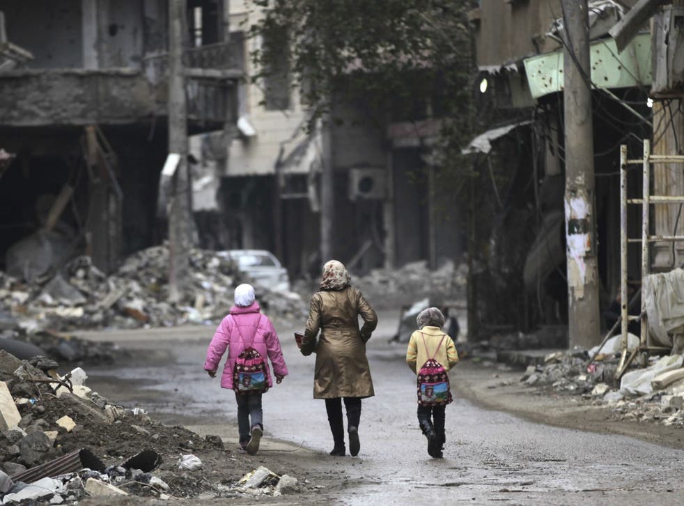 A woman walks with her children along a damaged street filled with debris in Deir al-Zor, eastern Syria 