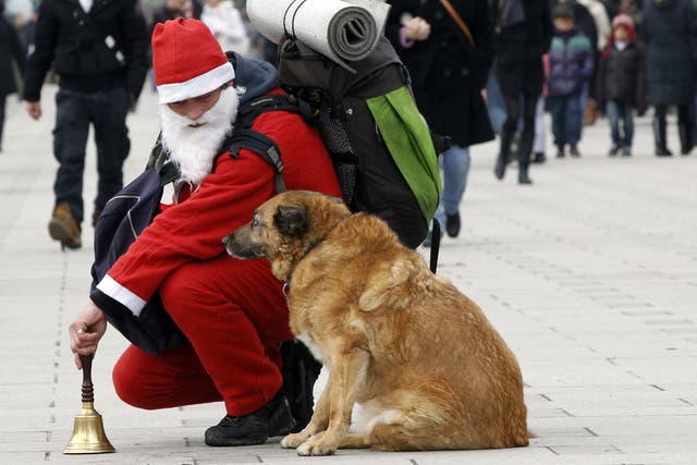 A homeless man dressed up as Santa Klaus looks at his dog in the Champs-Elysees in Paris