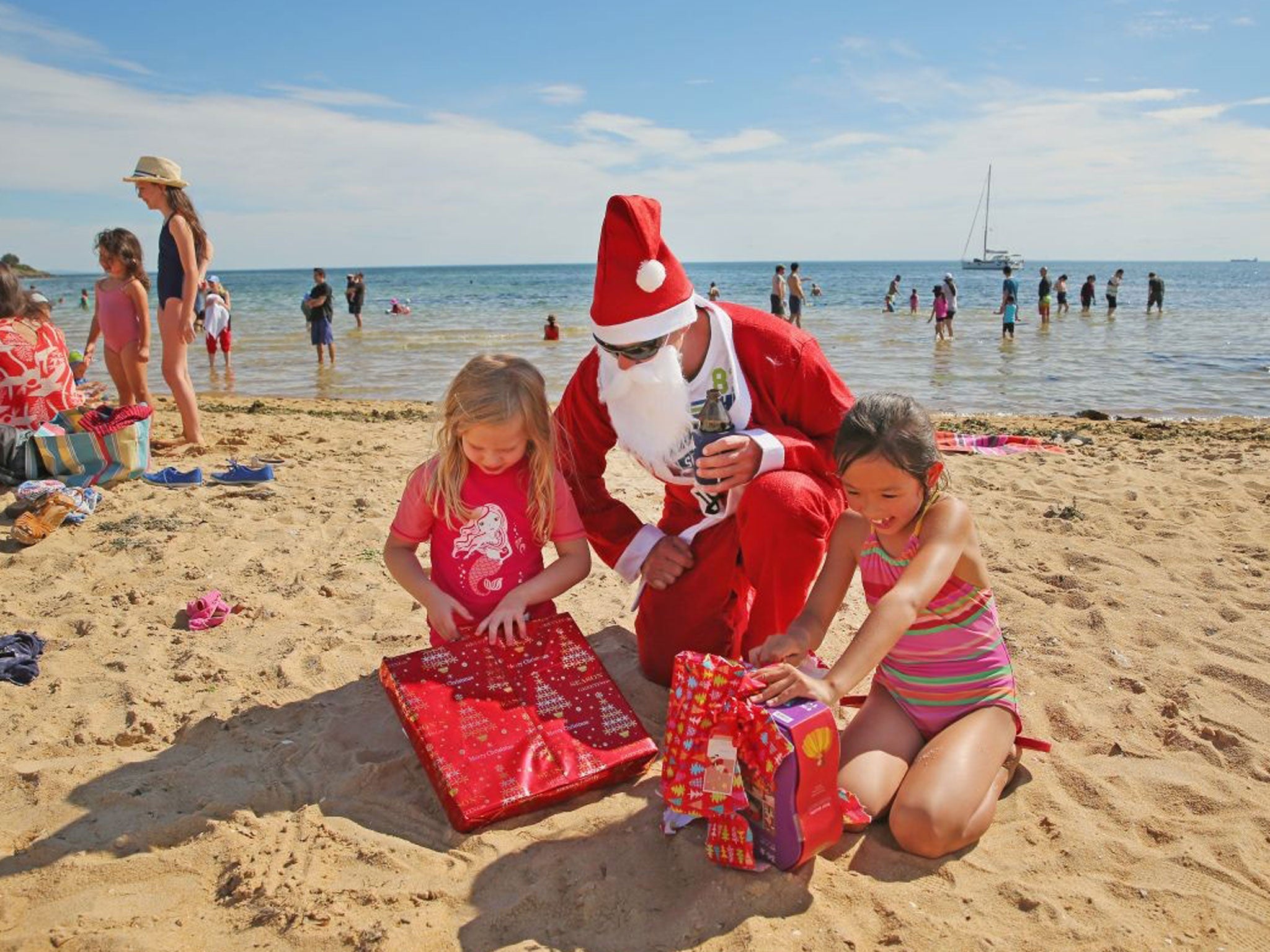 A casual Santa Claus helps children to open their Christmas presents on Christmas Day at Brighton Beach in Melbourne