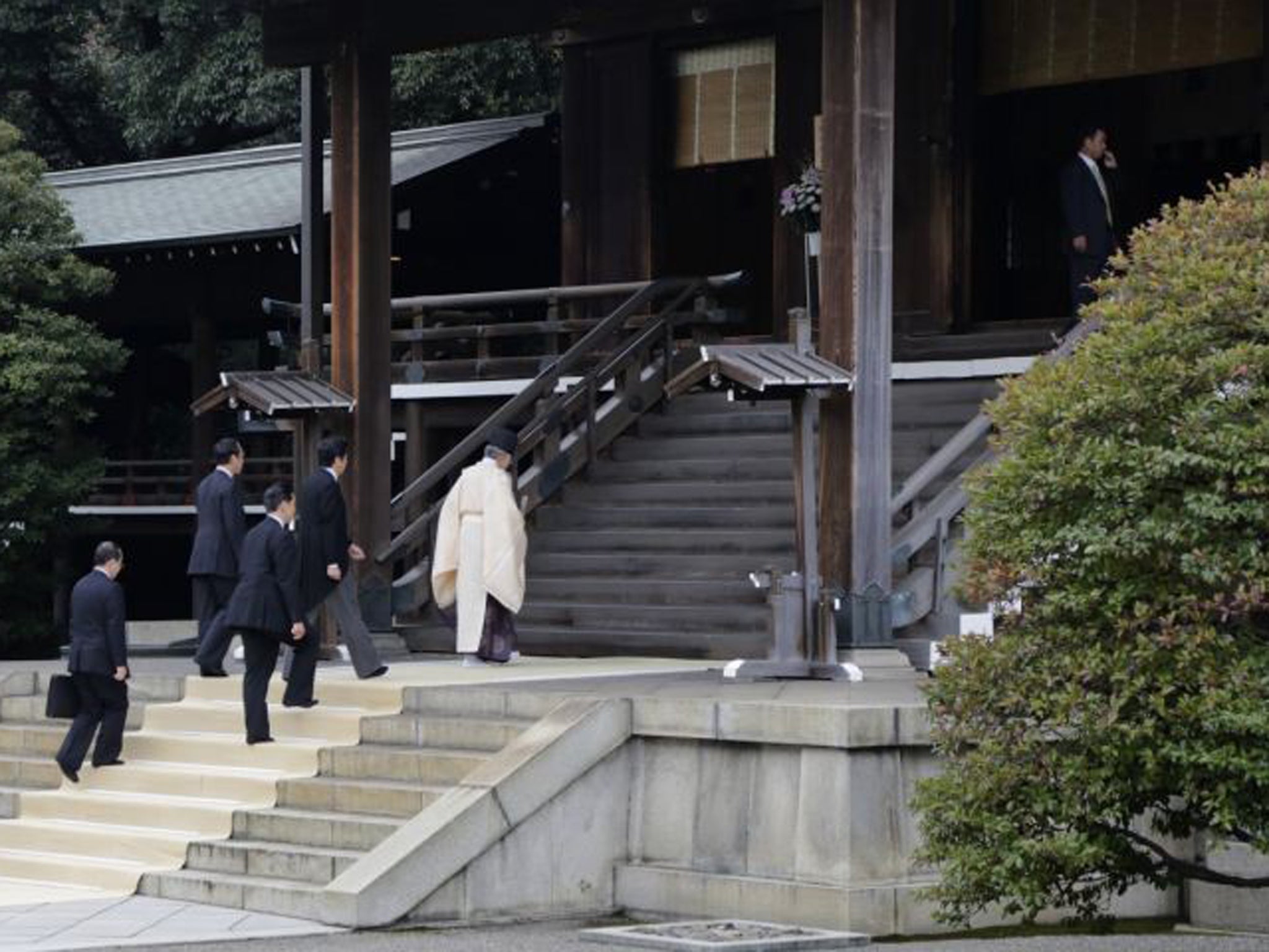 Japan's Prime Minister Shinzo Abe is led by a Shinto priest as he visits Yasukuni shrine in Tokyo