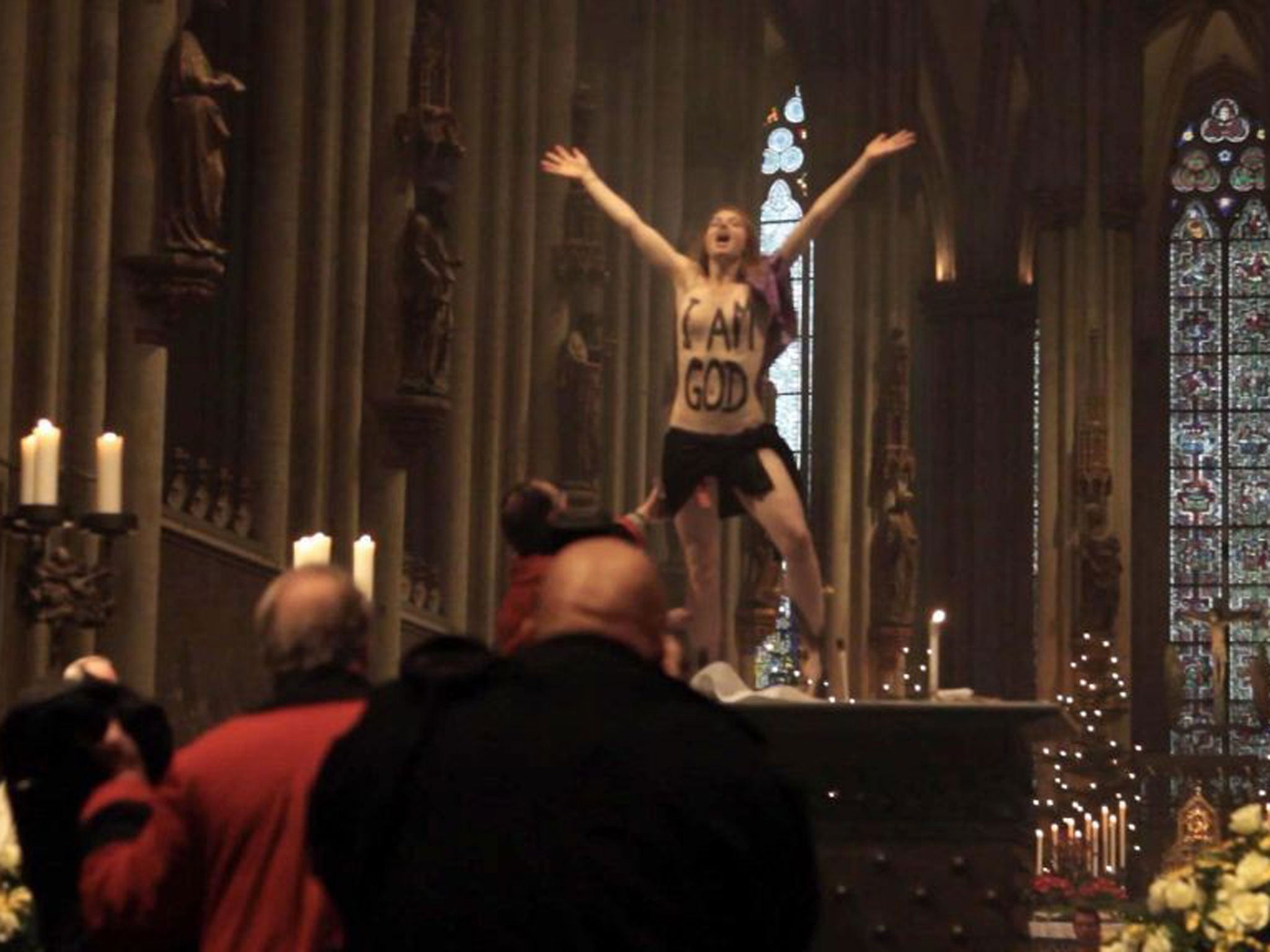 A topless Femen activist with the words 'I am God' painted on her chest stands on the altar during the Christmas Day service in Cologne Cathedral