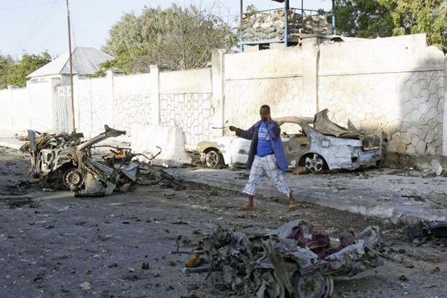 A man walks near the wreckage of cars after bombs went off at the gate of a hotel in Mogadishu