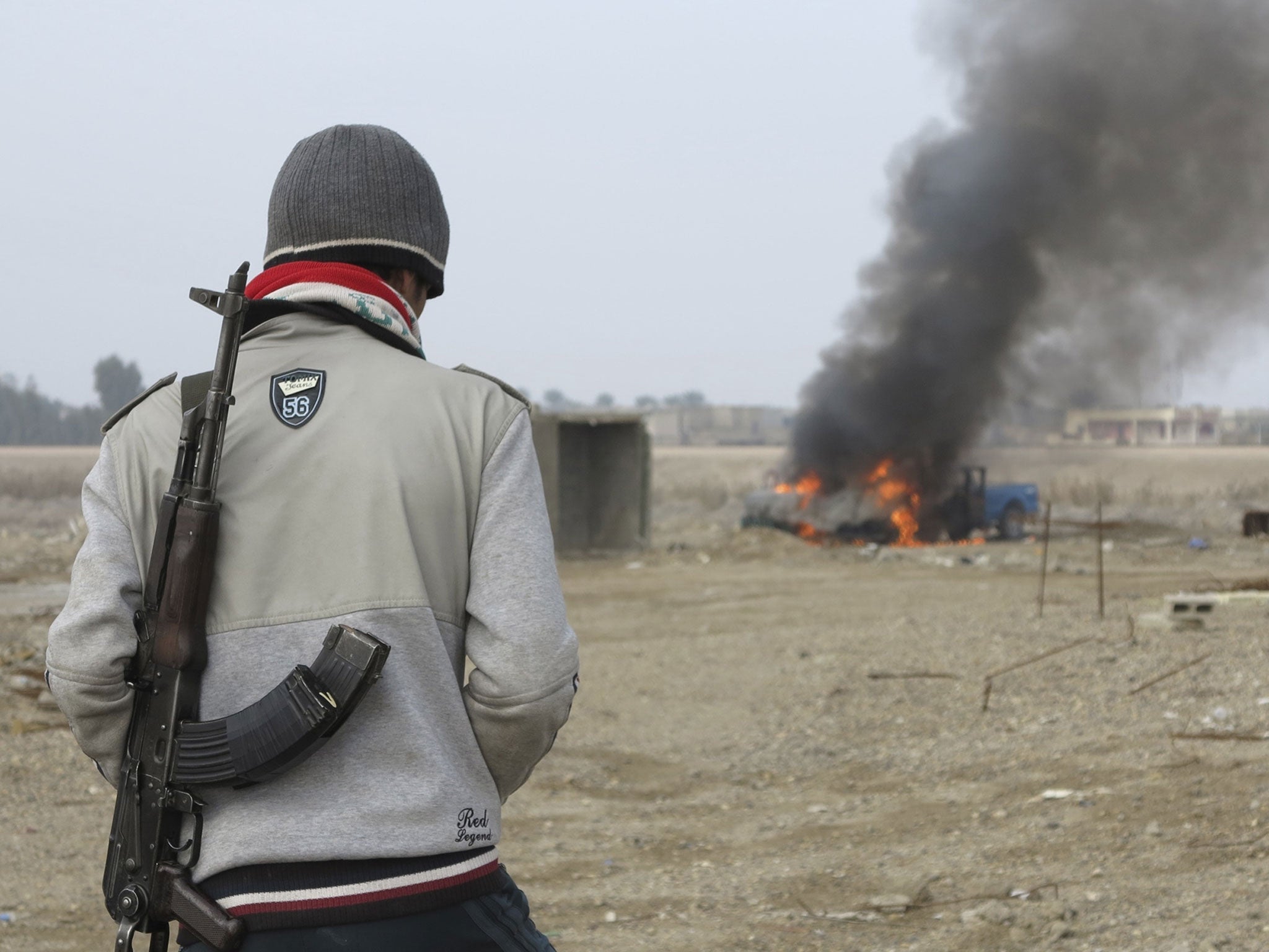 A Sunni Muslim fighter looks at a burning police vehicle during clashes in Ramadi
