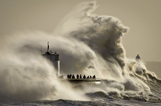 People watch and photograph enormous waves as they break on Porthcawl harbour