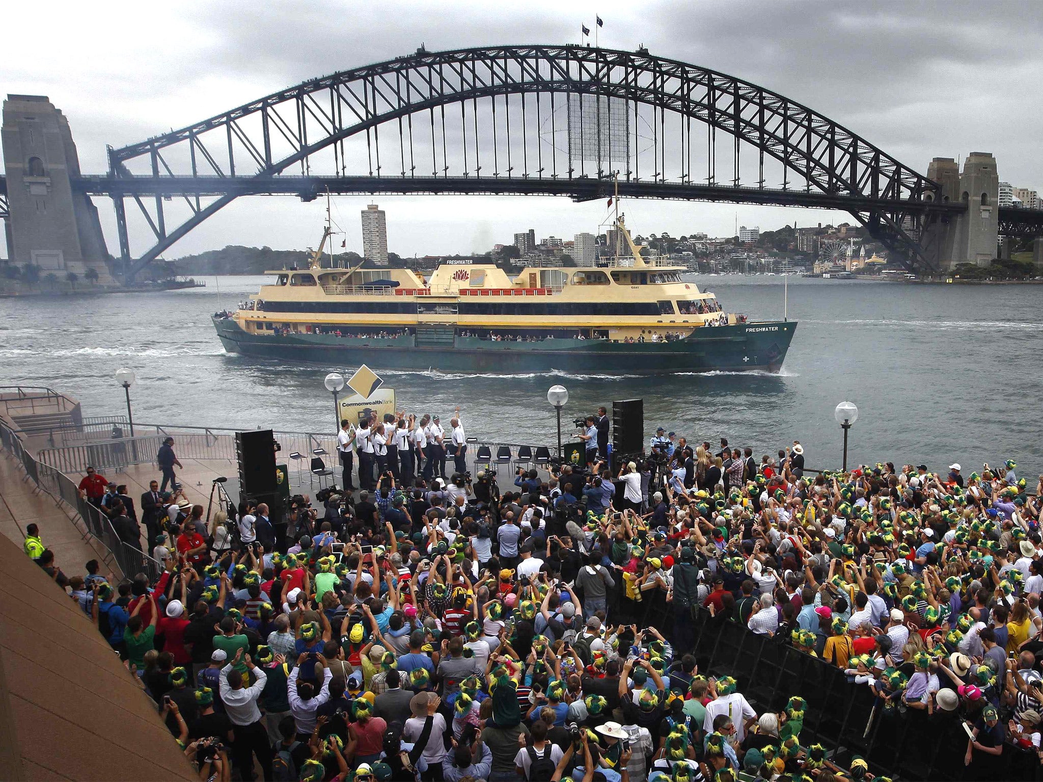 Members of the Australian cricket team wave to passengers sailing past on a ferry