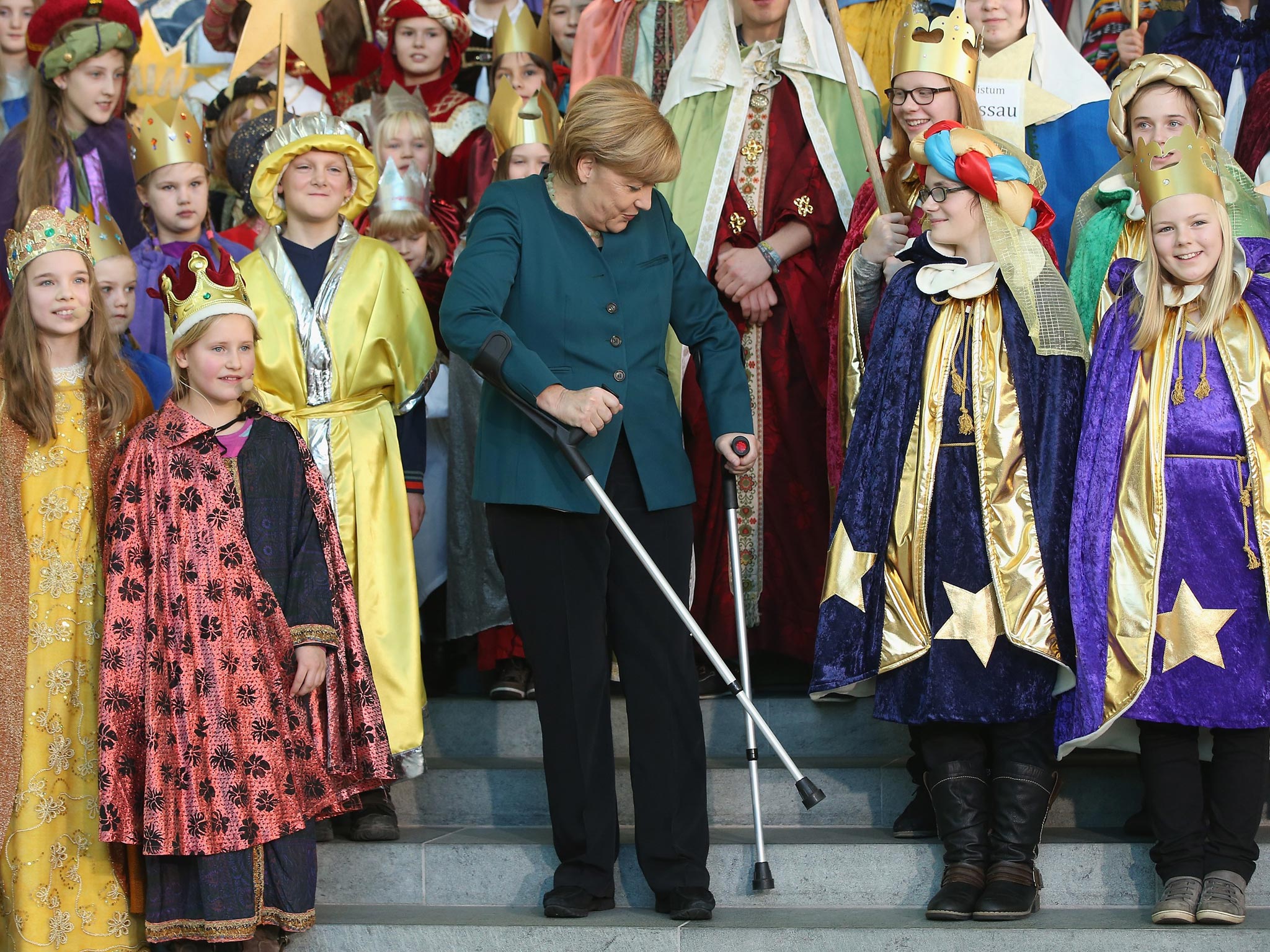 German Chancellor Angela Merkel stands with crutches as she attends a gathering of Epiphany child singers dressed as the Three Kings at the Chancellery
