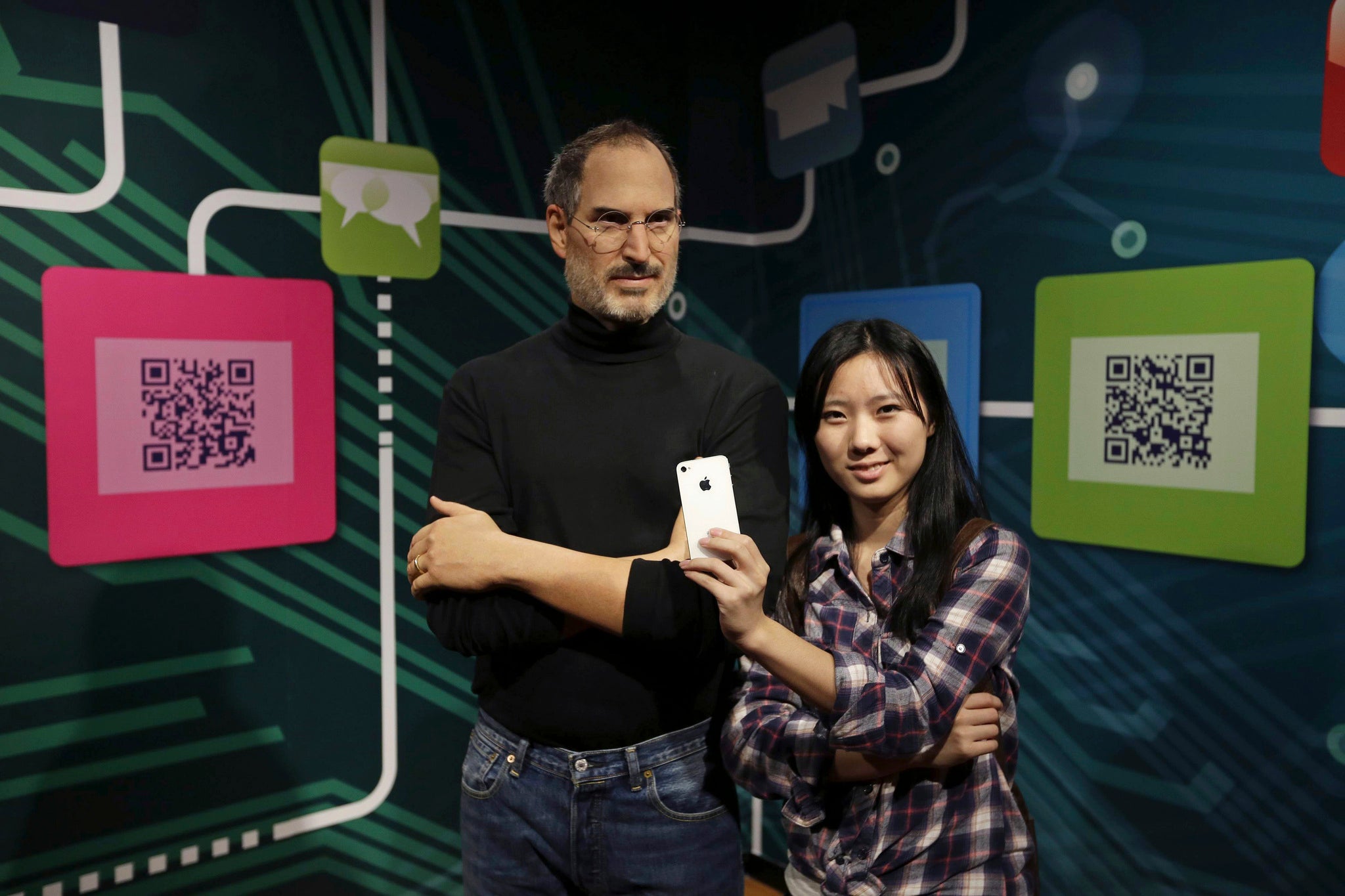 A woman poses for photographs with an iPhone next to a wax figure of Apple's co-founder Steve Jobs during a preview visit at a Madame Tussauds Museum in Wuhan, China.