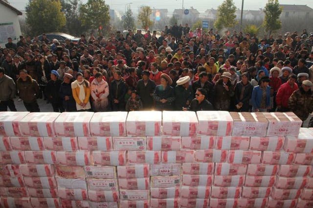 This picture taken on 14 January, 2014 shows villagers waiting before a two-metre-long "money wall" built with cash for their year-end bonus at Jianshe village of Lianshan municipality, southwest China's Sichuan province
