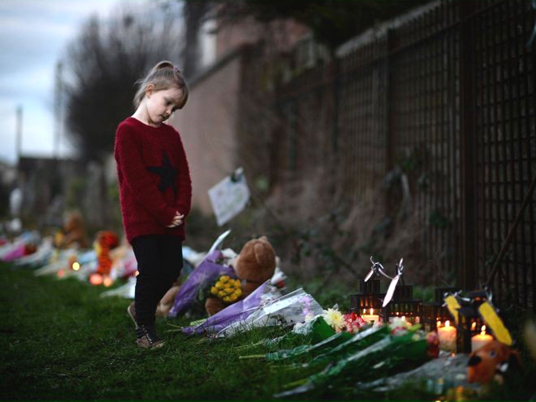 A young girl looks at flowers and candles laid by members of the public near to the house in Ferry Gait Crescent where 3 year-old Mikaeel Kular was reported missing in Kirkcaldy