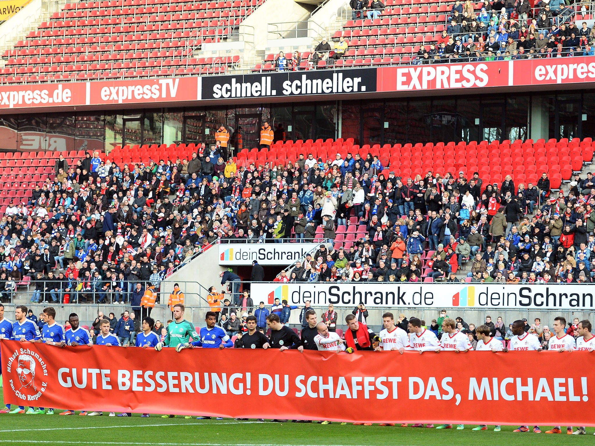 Players from Cologne (R) and Schalke (L) hold up a banner in tribute to Michael Schumacher, who is recovering from serious head injuries after a skiing accident
