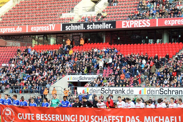 Players from Cologne (R) and Schalke (L) hold up a banner in tribute to Michael Schumacher, who is recovering from serious head injuries after a skiing accident